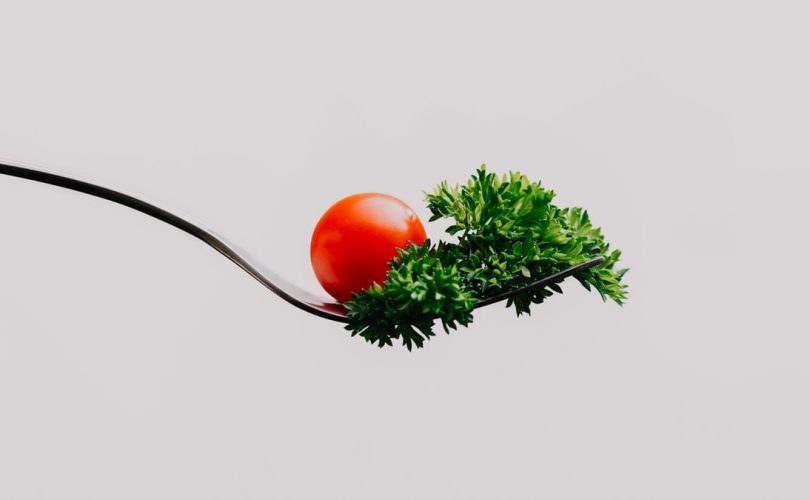 Minimalist close-up of a cherry tomato and parsley on a fork. Perfect for food design.